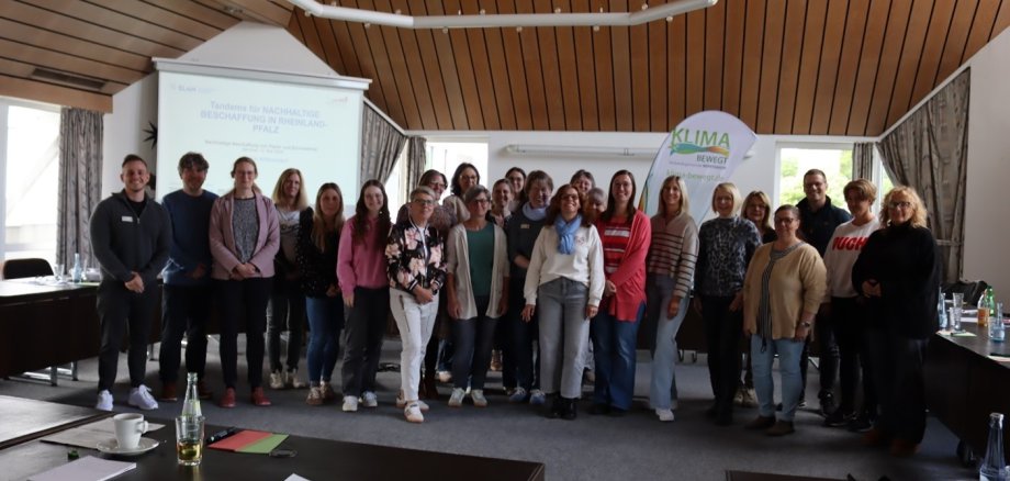Frauen und Männer stehen in einem Schulungsraum vor dem Aufsteller "Klima bewegt". 