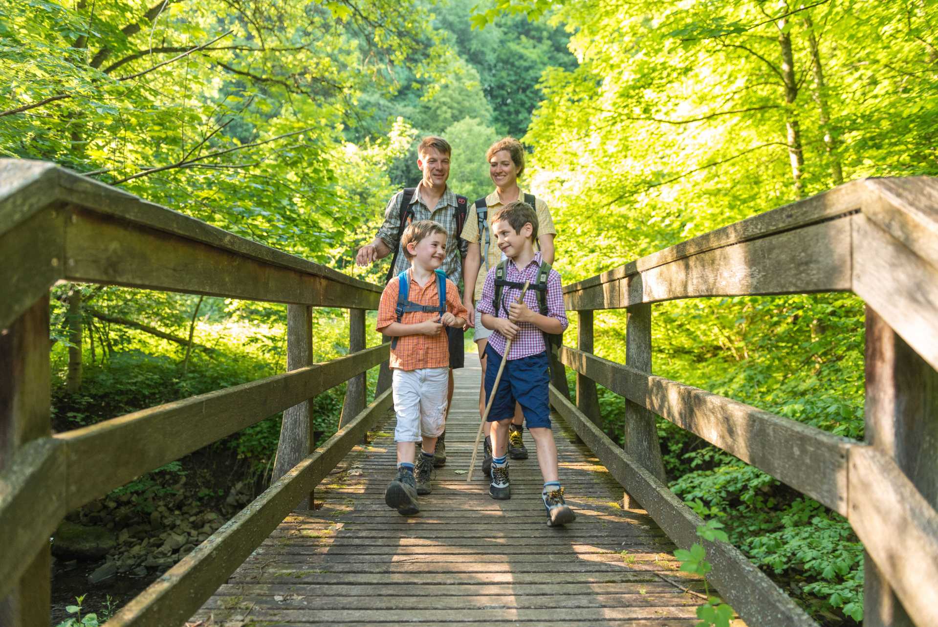 Eine Familie wandert über eine Holzbrücke im Wald.