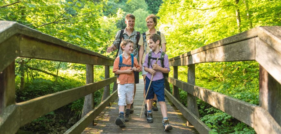 Eine Familie wandert über eine Holzbrücke im Wald.