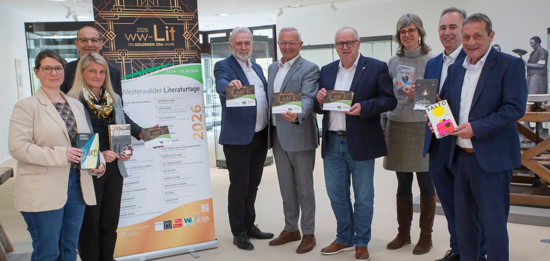 Frauen und Männer stehen mit einem Programmheft in der Hand vor einem Rollup mit der Aufschrift ww-Lit 2026.