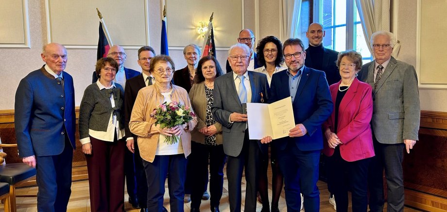 Frauen und Männer stehen vor drei Fahnen, einer mit Medaille und einer mit Urkunde.