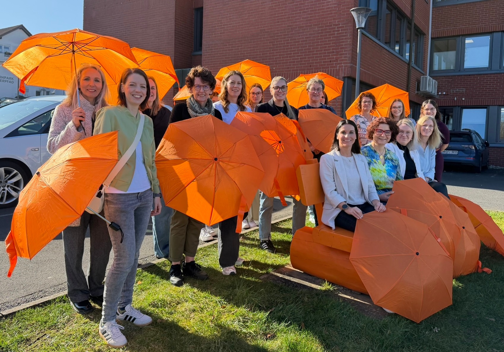 Eine orange Bank ist umringt von zahlreichen Frauen mit orangen Schirmen.