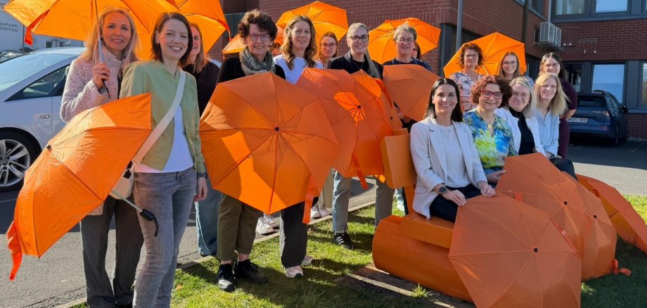 Eine orange Bank ist umringt von zahlreichen Frauen mit orangen Schirmen.