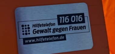 Auf einer Plakette steht Hilfetelefon "Gewalt gegen Frauen " 116016.