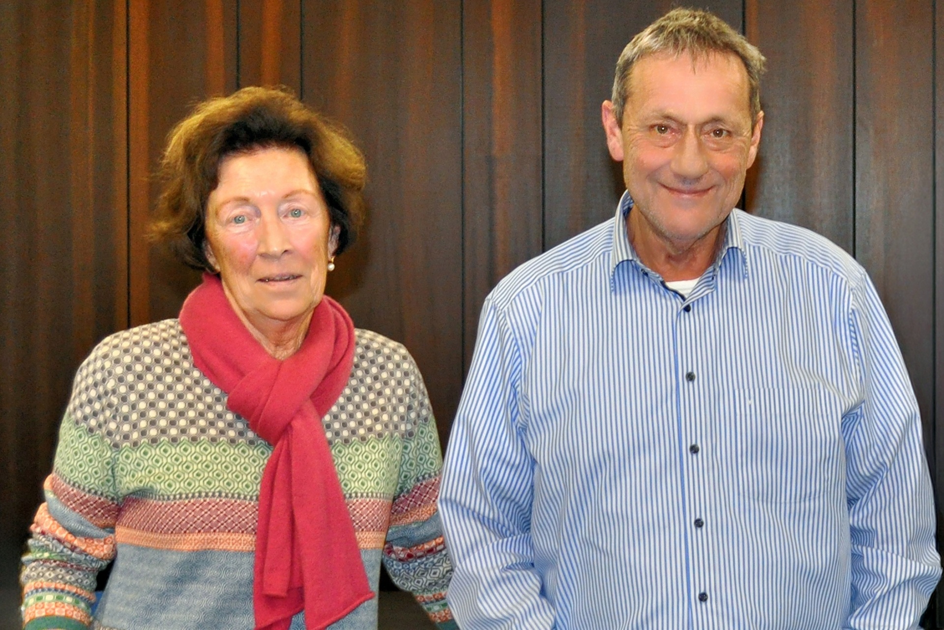 Eine Frau mit rotem Schal steht neben einem Mann im blau-gestreiften Hemd.
