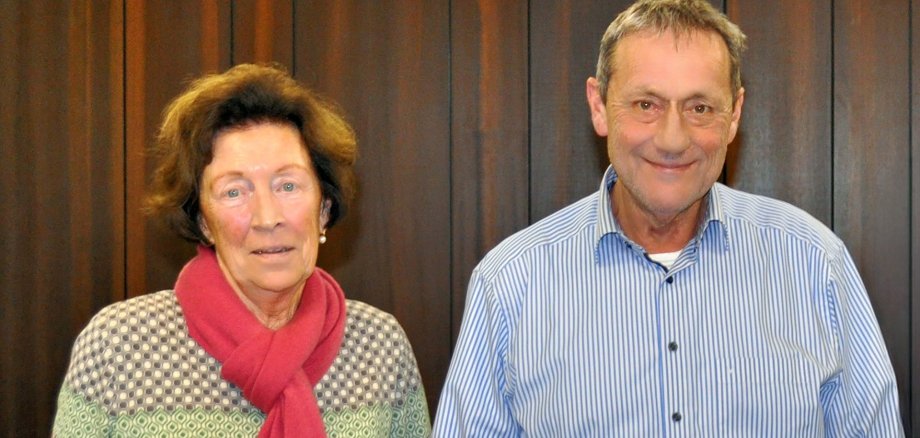 Eine Frau mit rotem Schal steht neben einem Mann im blau-gestreiften Hemd.