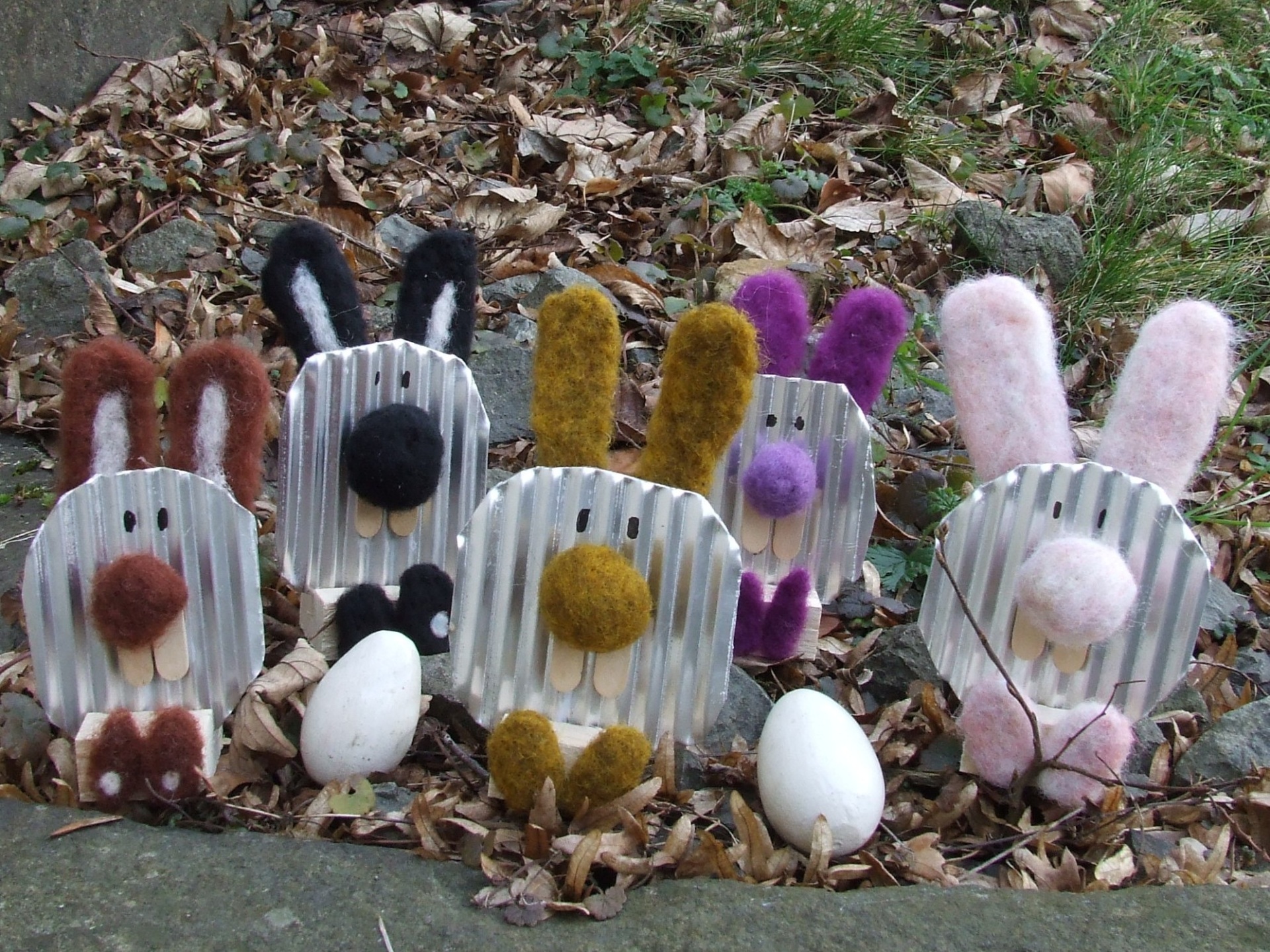 Aus Blech gebastelte Hasen mit Filzohren sitzen auf einer Wiese.