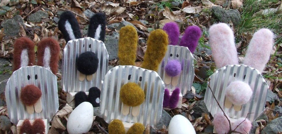 Aus Blech gebastelte Hasen mit Filzohren sitzen auf einer Wiese.