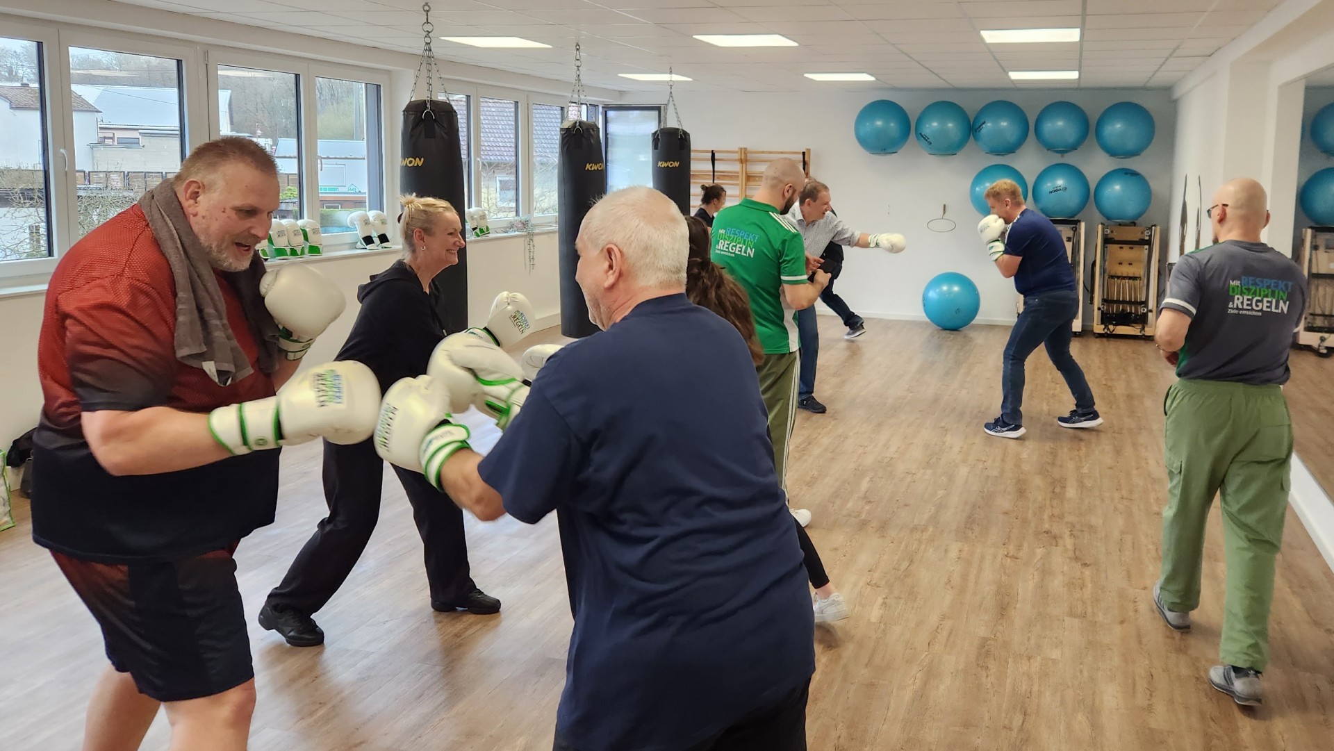 Männer und Frauen mit Boxhandschuhen trainieren unter Anleitung.