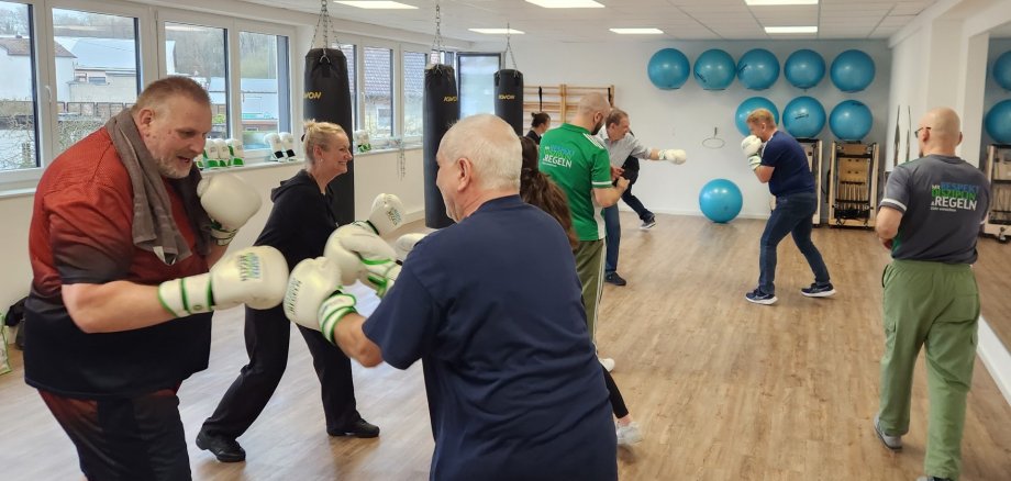 Männer und Frauen mit Boxhandschuhen trainieren unter Anleitung.