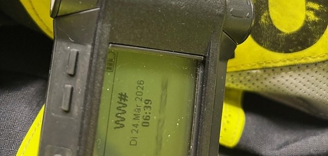Ein digitaler Funkmeldeempfänger steht liegt vor einer Feuerwehrjacke.