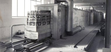 Schwarz-Weiß-Aufnahme einer Keramikfabrik mit großen Maschinen und vielen Vasen.