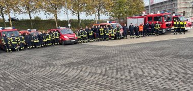 Auf einem Parkplätze stehen Feuerwehrfahrzeuge und Feuerwehrleute.