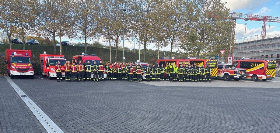 Auf einem Parkplätze stehen Feuerwehrfahrzeuge und Feuerwehrleute.