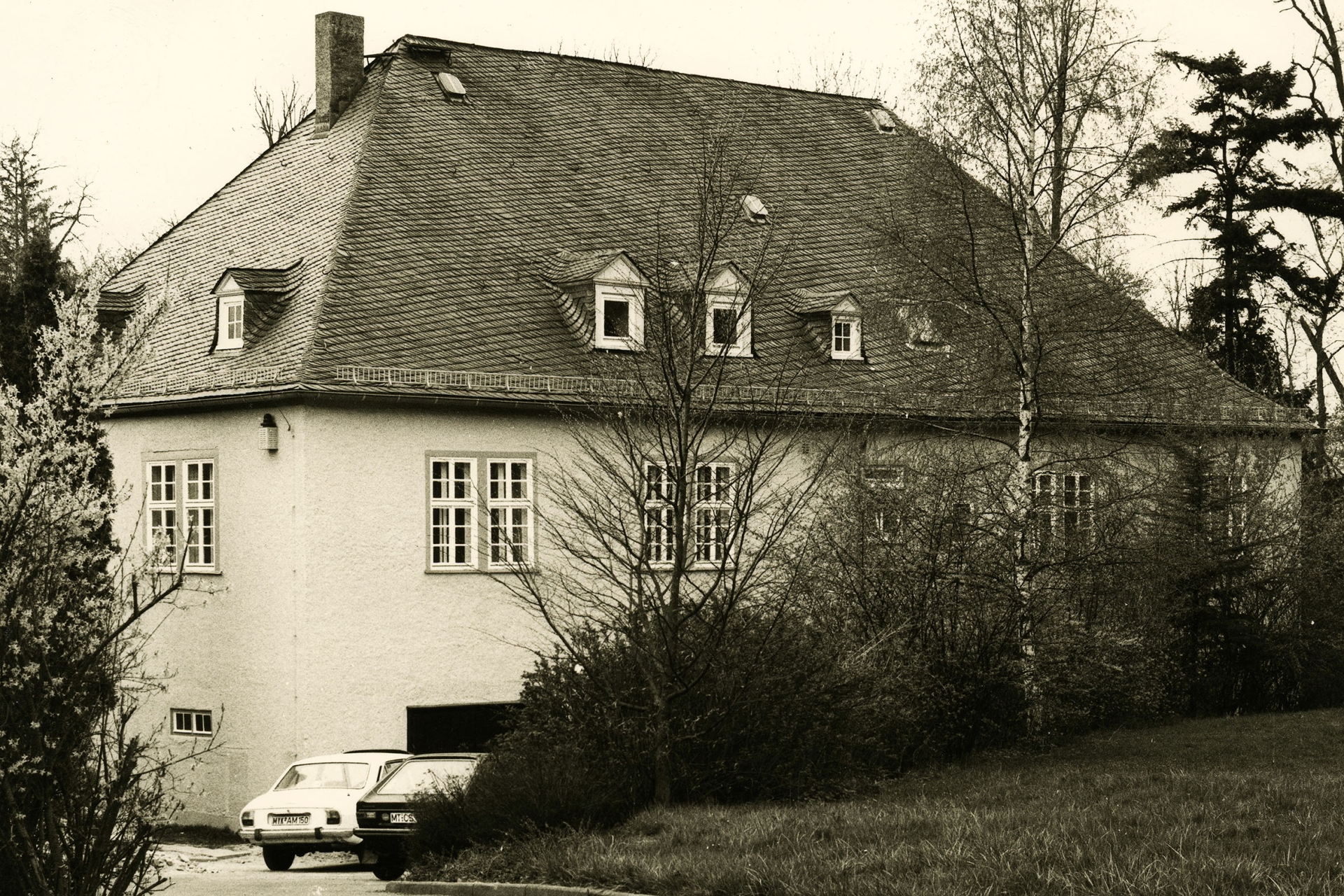 Ein großes Haus, umgeben von Bäumen, in schwarz-weiß.