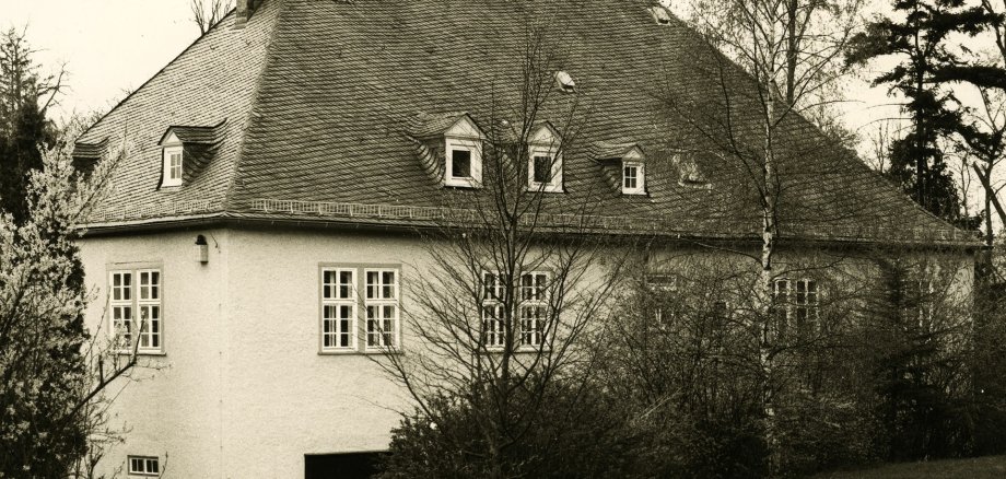 Ein großes Haus, umgeben von Bäumen, in schwarz-weiß.