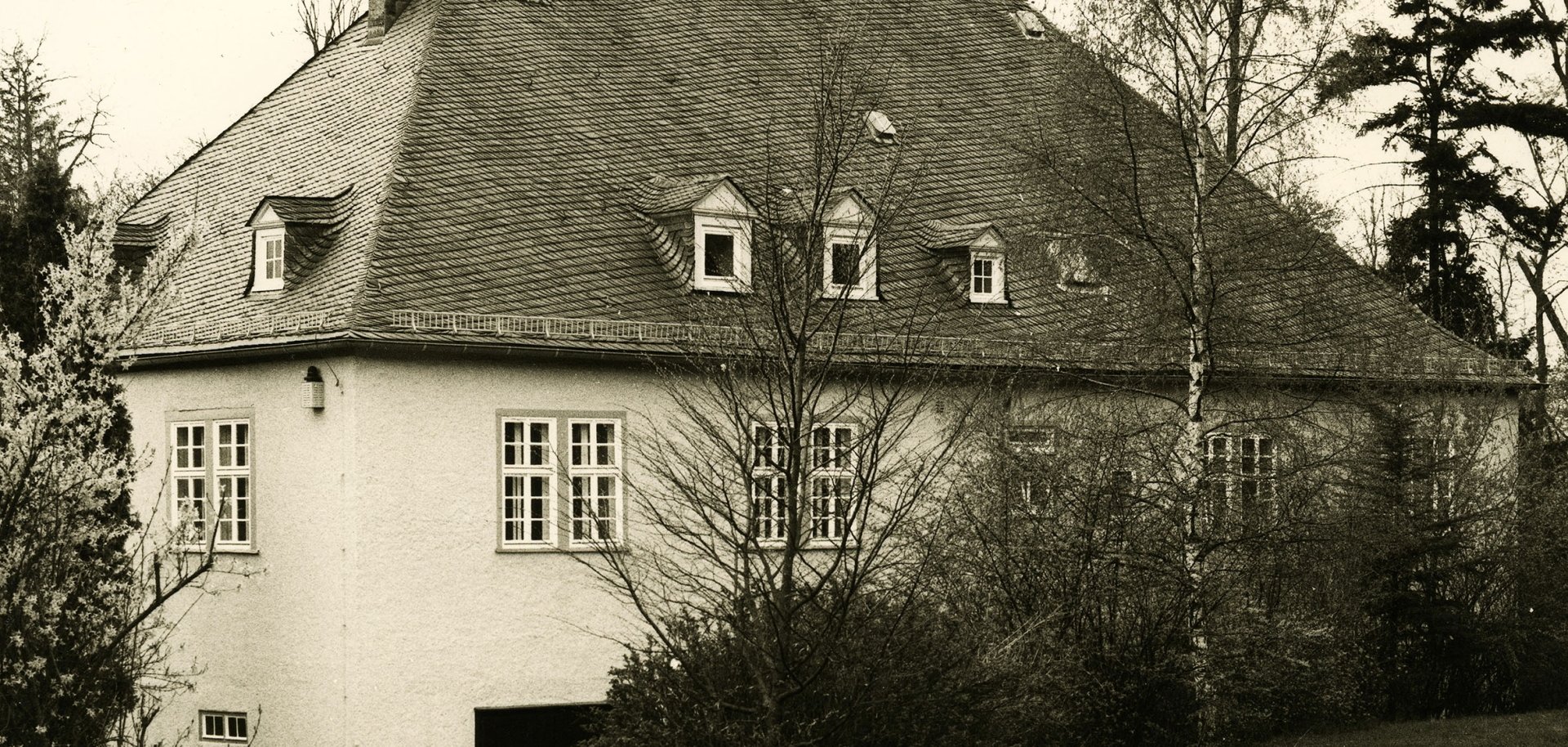 Ein großes Haus, umgeben von Bäumen, in schwarz-weiß.