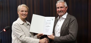 Eine Frau überreicht einem Mann mit Handschlag eine Urkunde.