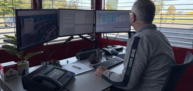 Ein Mann sitzt am Schreibtisch vor vielen Monitoren.