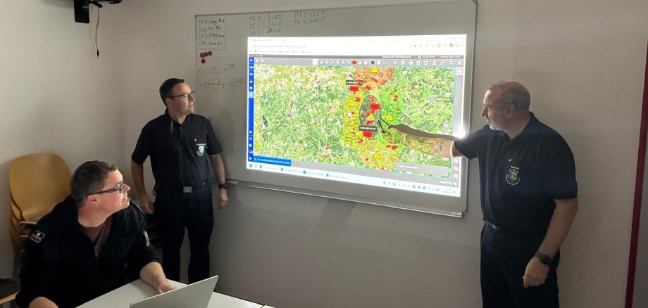 Männer zeigen auf eine Lagekarte an der Wand.
