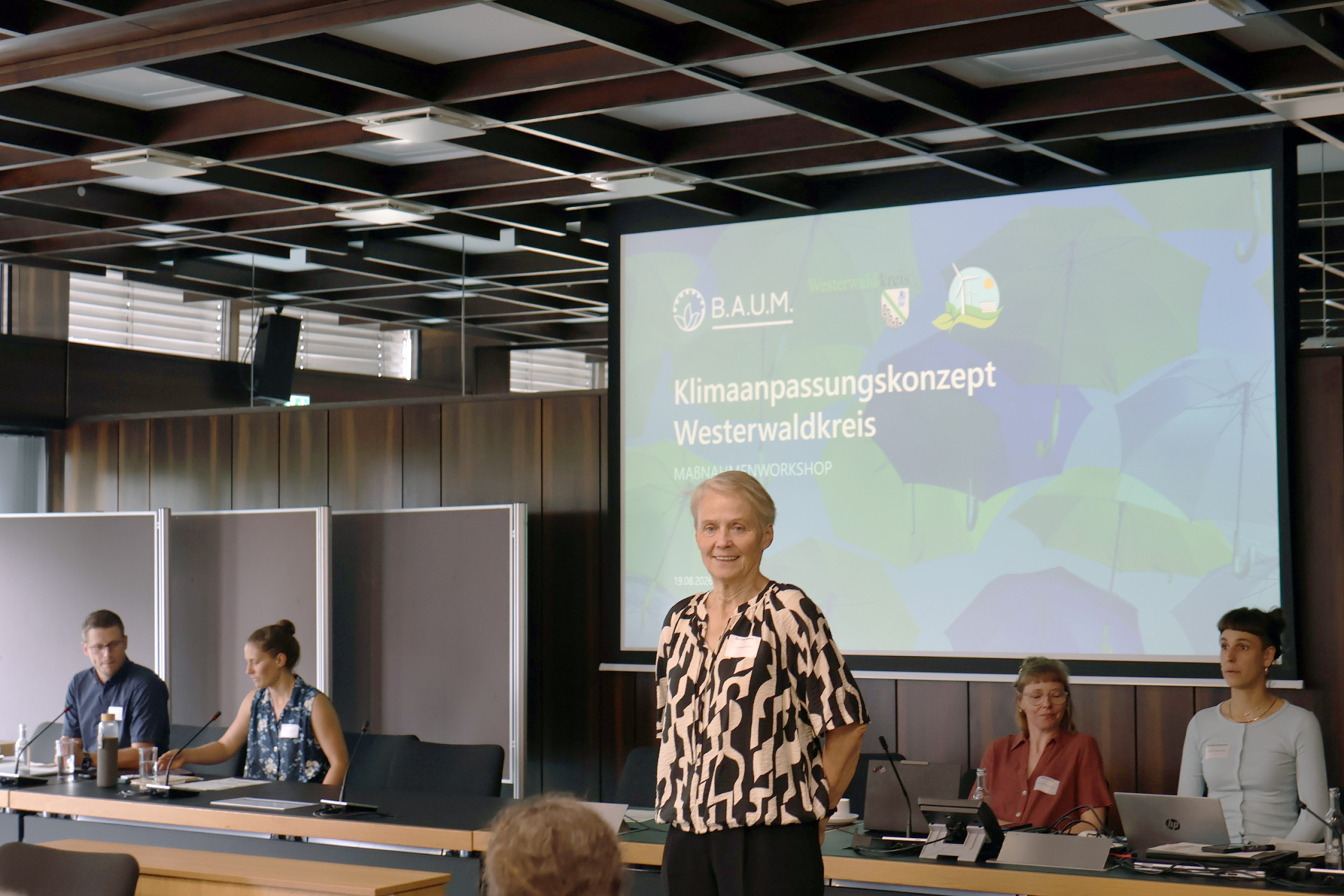 Eine Frau steht vor einer Präsentation mit dem Titel Klimaanpassungskonzept.