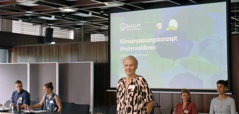 Eine Frau steht vor einer Präsentation mit dem Titel Klimaanpassungskonzept.