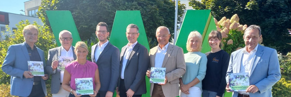 Mehrere Frauen und Männer stehen vor einem großen grünen W mit einem Flyer von WesterwaldTalents in der Hand.