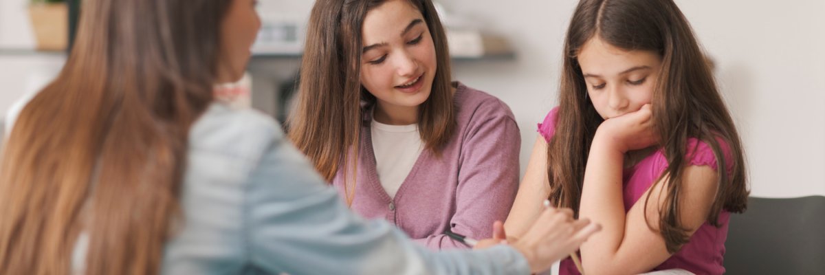 Eine junge Frau hilft Kindern bei den Hausaufgaben.
