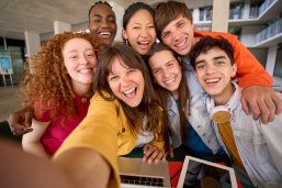 Eine Gruppe junger Leute unterschiedlicher Herkunft macht ein Selfie in einer Bibliothek.