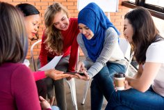 Eine multikulturelle Frauengruppe schaut auf ein Tablet.