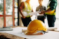 Ein Ingenieurteam mit Schutzhelmen trifft sich auf einer Baustelle zu einer Besprechung.