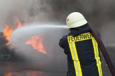 Ein Feuerwehrmann steht vor einer schwarzen Rauchwolke und löscht.