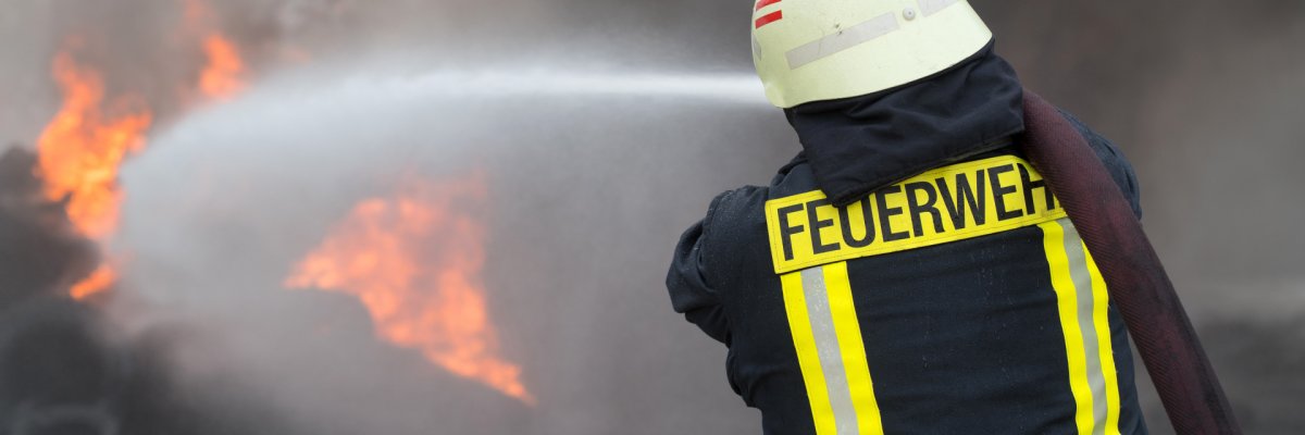 Ein Feuerwehrmann steht vor einer schwarzen Rauchwolke und löscht.