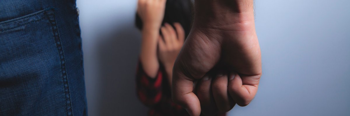 Ein Mann ballt seine Faust vor einer zusammengekauerten Person im Hintergrund.