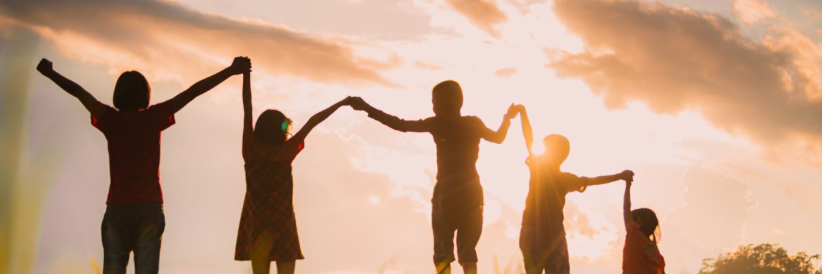 Mit einem Sonnenuntergang im Hintergrund halten sich fünf Kinder an den Händen.