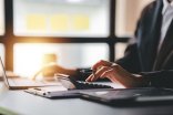 Eine Frau arbeitet an einem Tisch mit Computer, Taschenrechner und Stift.