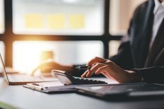 Eine Frau arbeitet an einem Tisch mit Computer, Taschenrechner und Stift.