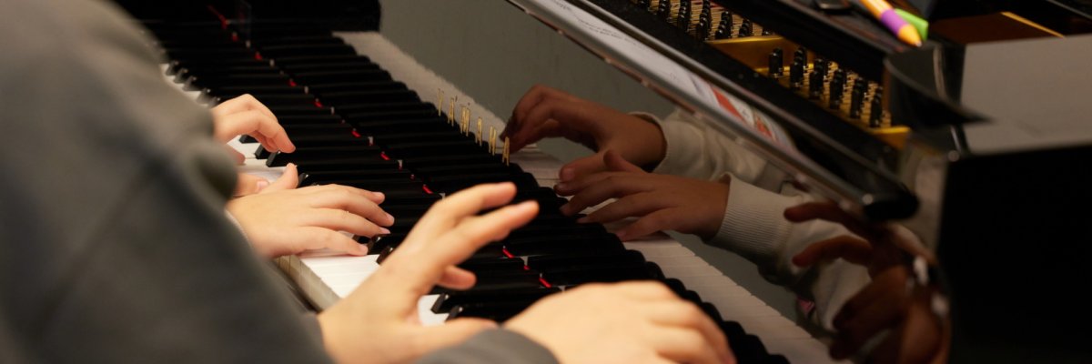 Vier Hände spielen auf einem schwarzen Klavier.