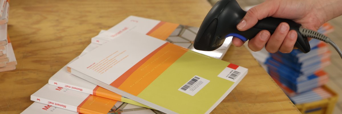 Bücher liegen auf einem Tisch und werden per Handscanner gescannt.
