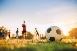 Die Silhouten von Kindern spielen auf Rasen Fußball.
