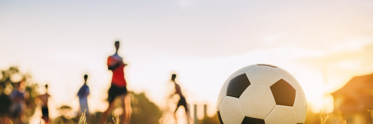 Die Silhouten von Kindern spielen auf Rasen Fußball.