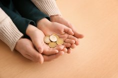 Hände eines Erwachsenen und eines Kindes halten Münzen.
