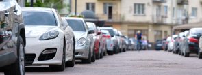 Eine Straße an der links und rechts jeweils parkende Autos stehen.