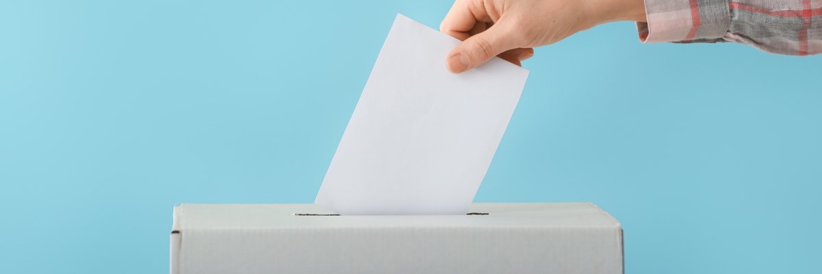 Eine Hand steckt einen Wahlzettel in eine Urne.