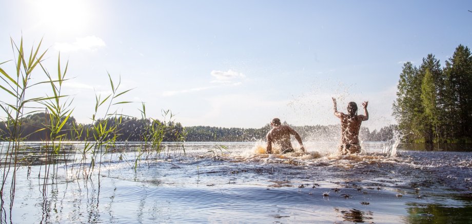 Ein Mann und eine Frau spritzen mit Wasser in einem Badesee an einem heißen Sommertag.