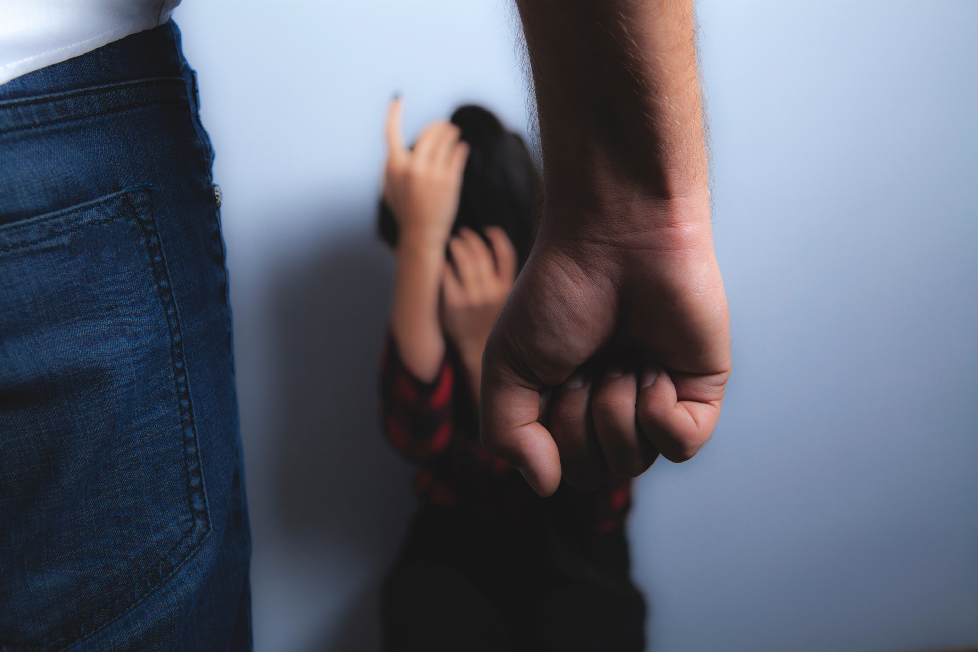 Ein Mann ballt seine Faust vor einer zusammengekauerten Person im Hintergrund.