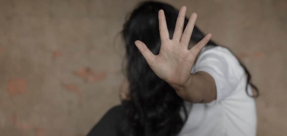 Eine Frau versteckt ihr Gesicht und hält eine Hand zur Abwehr Richtung Kamera.