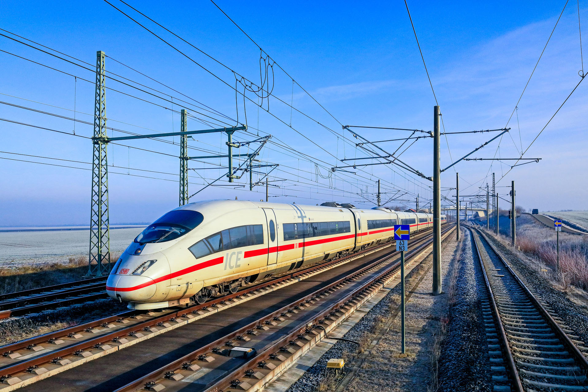 Unterwegs auf der VDE 8.1 Auf Gleisen und mit Hochspannungsleitungen fährt ein weißer ICE mit rotem Streifen.