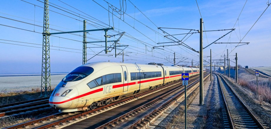 Auf Gleisen und mit Hochspannungsleitungen  fährt ein weißer ICE mit rotem Streifen.