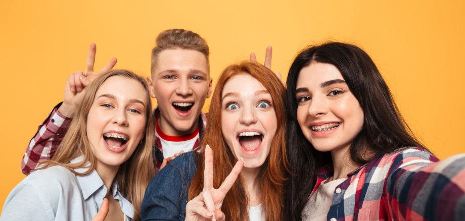 Eine Gruppe von Teenagern lacht in die Kamera vor einen bunten Hintergrund.
